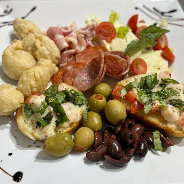 A white plate with an assortment of Italian appetizers including bruschetta, olives, and cured meats.