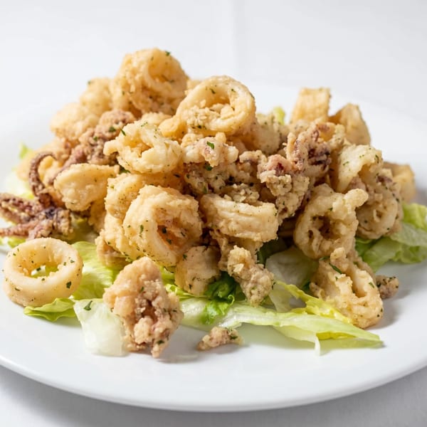 Crispy fried calamari rings and tentacles, lightly seasoned, served on a bed of fresh green lettuce.