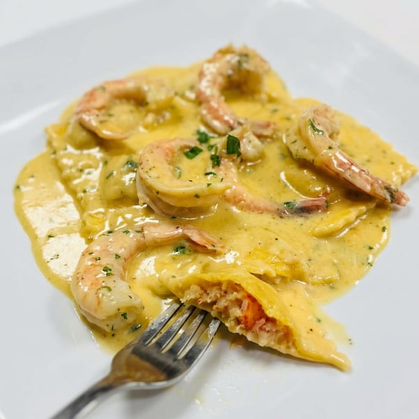 Shrimp ravioli in a creamy sauce with a fork cutting into one, revealing a lobster filling.
