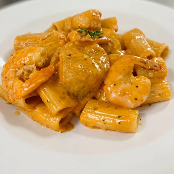 Rigatoni pasta with shrimp in a creamy orange sauce, garnished with fresh herbs.