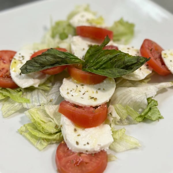 Caprese salad with fresh mozzarella, sliced tomatoes, basil, and lettuce on a white plate.