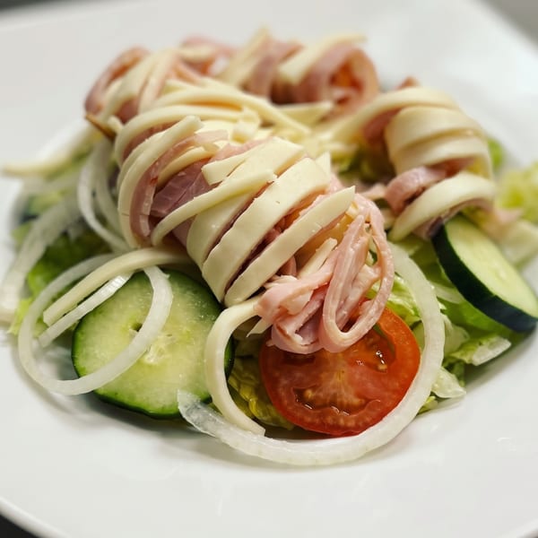 Fresh salad with ham and cheese rolls, sliced cucumbers, tomatoes, and onions on a white plate.
