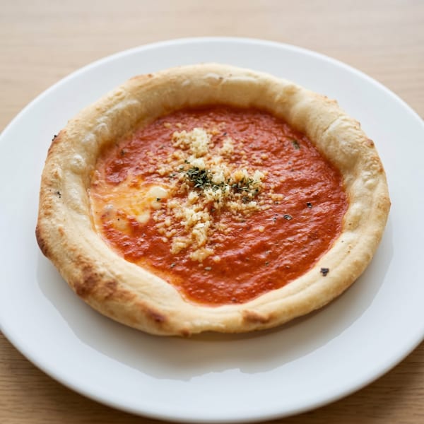 A small, round pizza with thick crust, red sauce, and crumbled toppings on a white plate.